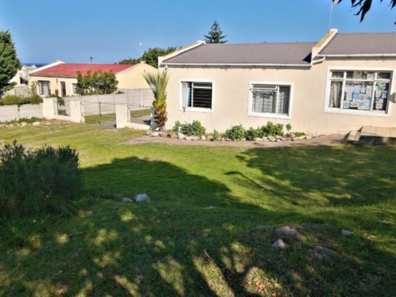 Rear view of the property featuring a lawn, concrete boundary wall, and metal roof structure.