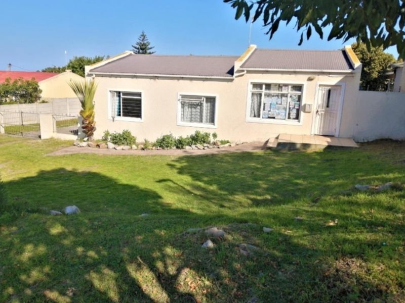 Front view of a single-story residential house featuring a corrugated metal roof, plastered exterior walls, and a small front garden area.
