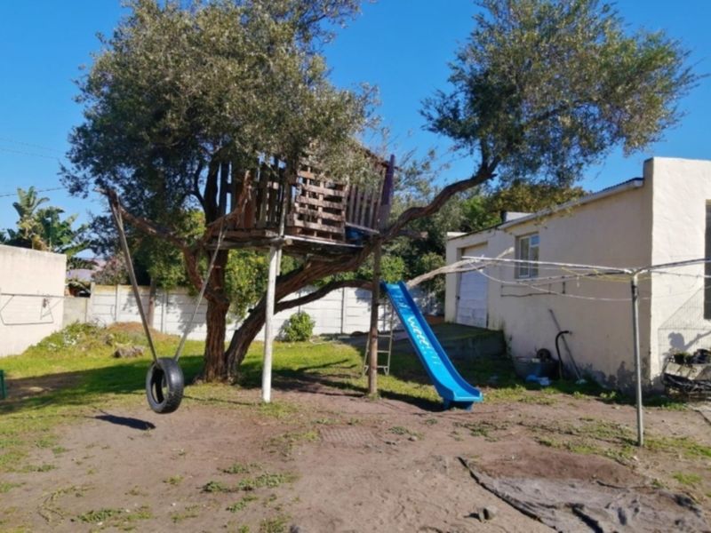 A spacious rear garden area featuring a treehouse, a tire swing, and a precast concrete boundary wall, offering potential for landscaping and outdoor improvement.
