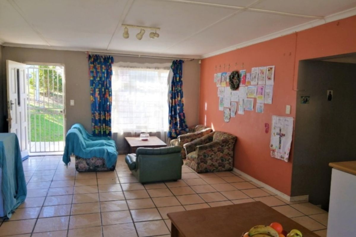 A living room area featuring tiled flooring, a security gate entrance, and natural light, offering a functional space ready for cosmetic updates.