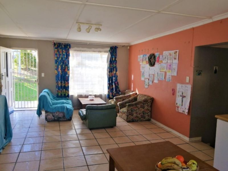 A living room area featuring tiled flooring, a security gate entrance, and natural light, offering a functional space ready for cosmetic updates.