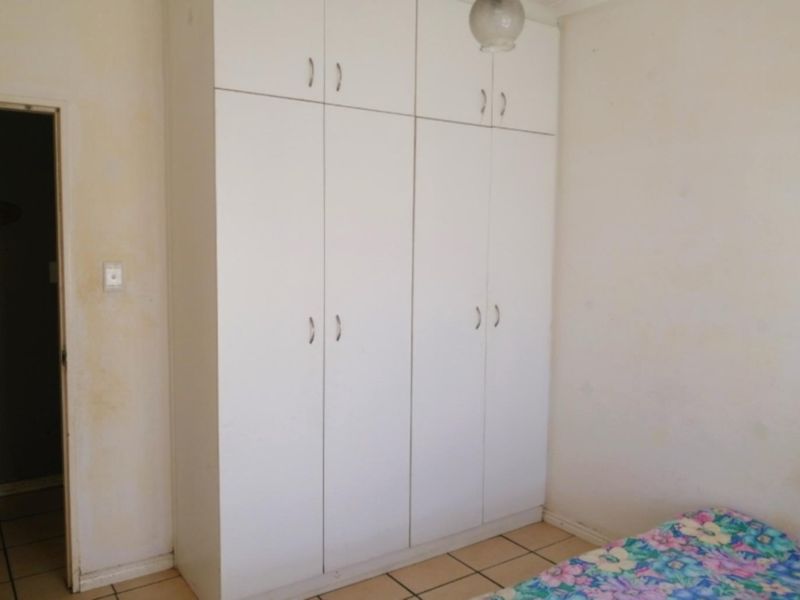 A bedroom featuring built-in white cupboards and tiled flooring, requiring minor cosmetic updates to the wall finishes.