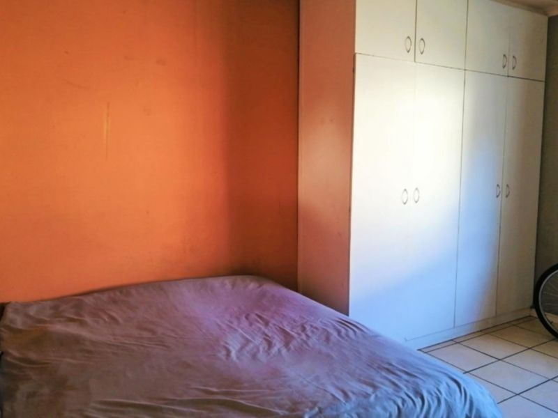 A bedroom featuring built-in cupboards and tiled flooring, currently requiring cosmetic updates to the wall finishes.