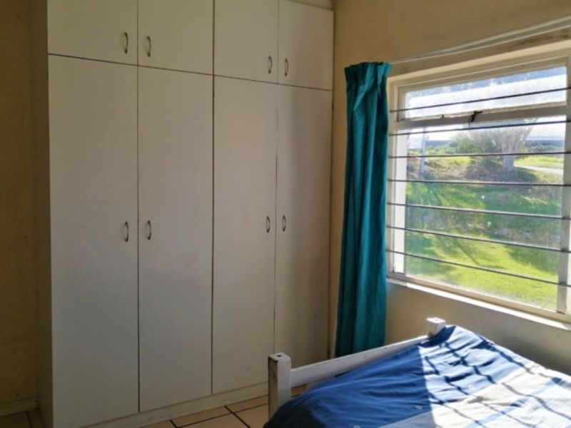 A bedroom featuring built-in cupboards, tiled flooring, and a steel-framed window with natural light.