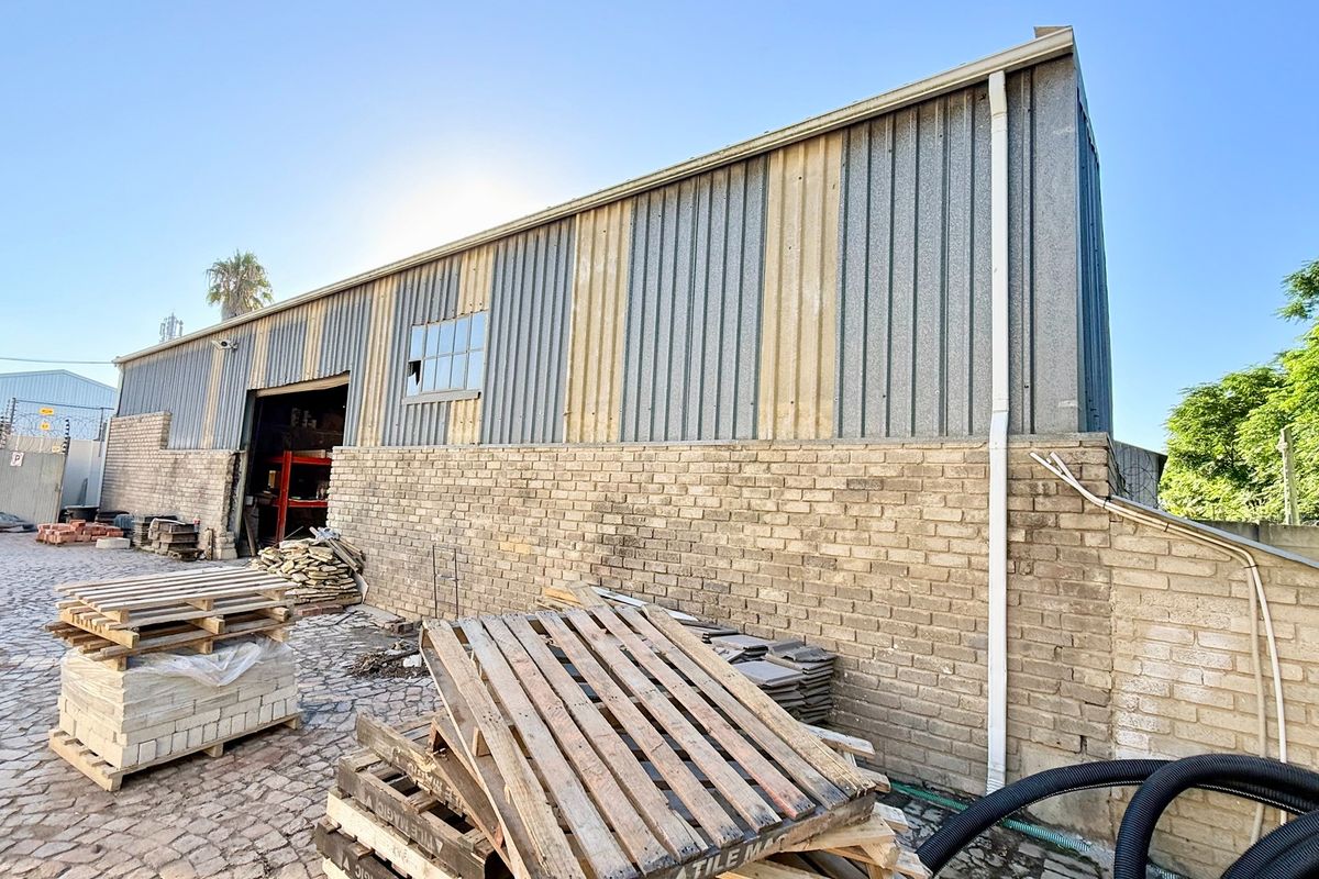 Rear exterior view of an industrial warehouse featuring corrugated metal cladding, brick masonry walls, and a paved yard area.