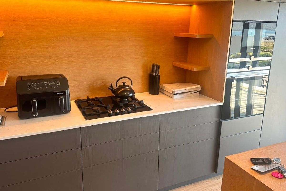Modern kitchen featuring dark cabinetry, stone countertops, a built-in gas cooktop, and integrated oven with warm under-cabinet lighting.
