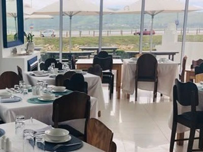 Bright restaurant dining area featuring large floor-to-ceiling windows with scenic views, tiled flooring, and a built-in fireplace.