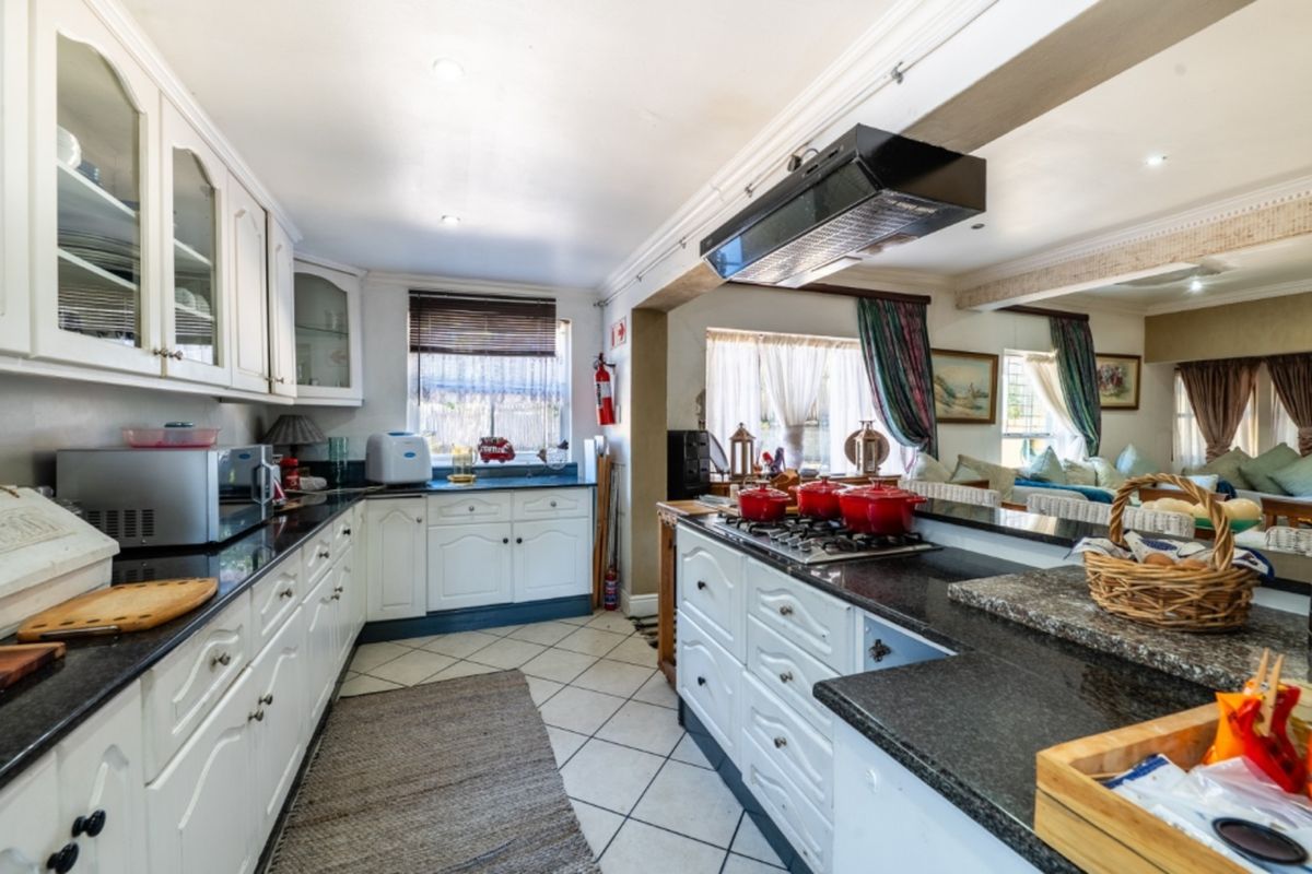A well-appointed kitchen featuring granite countertops, white cabinetry, a gas hob with an extractor fan, and tiled flooring, seamlessly flowing into the living area.