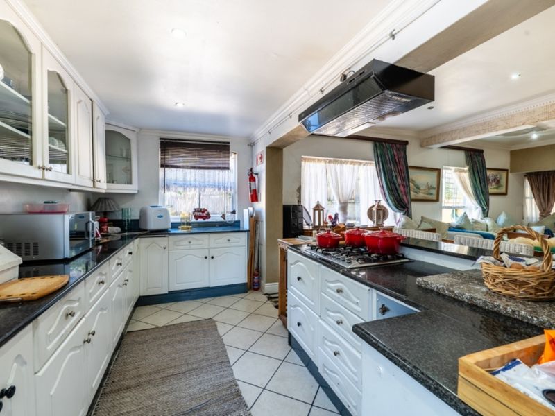 A well-appointed kitchen featuring granite countertops, white cabinetry, a gas hob with an extractor fan, and tiled flooring, seamlessly flowing into the living area.
