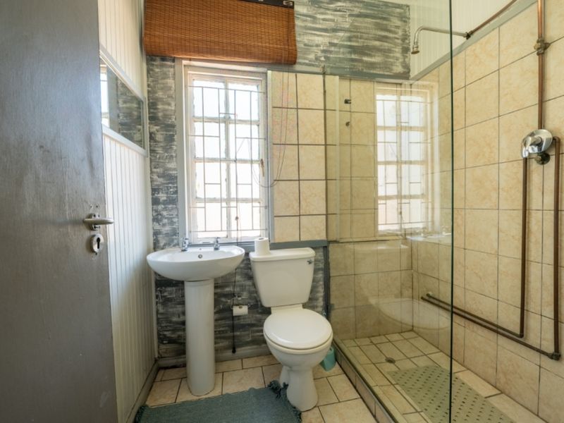 A functional bathroom featuring a pedestal basin, toilet, and a glass-enclosed shower with exposed copper piping and tiled finishes.