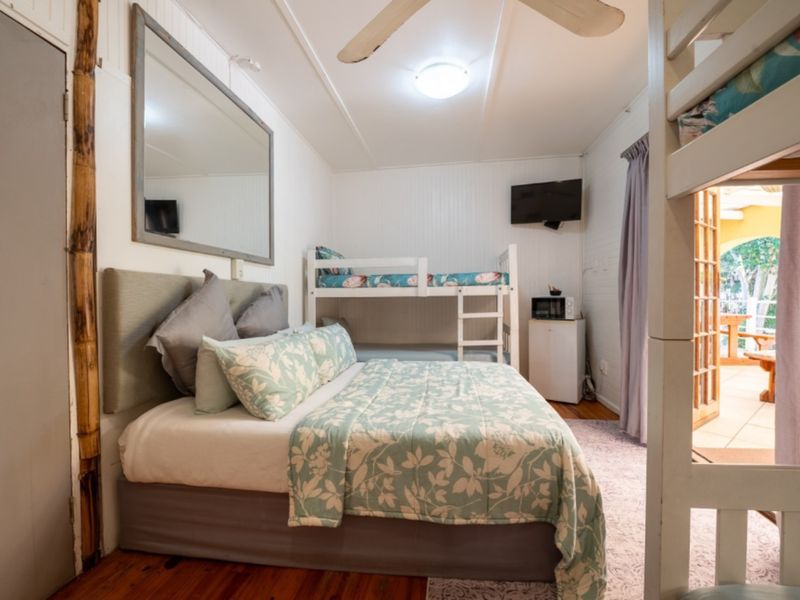 A functional bedroom featuring timber flooring, beadboard wall paneling, a ceiling fan, and direct access to an outdoor patio area through french doors.