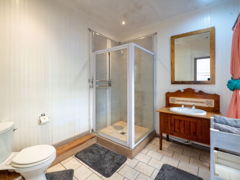A functional bathroom featuring a corner shower, vanity unit with basin, and toilet, finished with timber wall paneling and tiled flooring.
