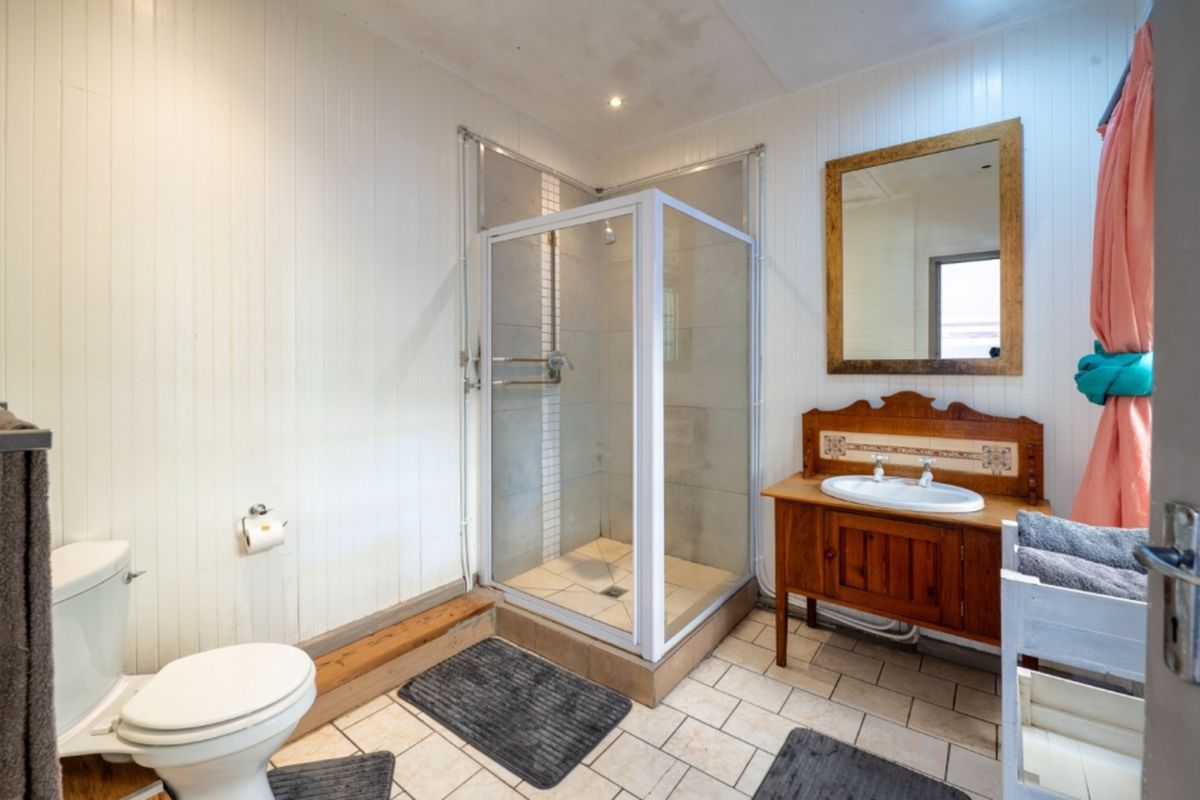 A functional bathroom featuring a corner shower, vanity unit with basin, and toilet, finished with timber wall paneling and tiled flooring.