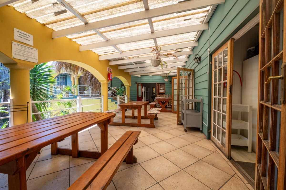 A covered outdoor patio area featuring tiled flooring, timber weatherboard walls, and a translucent roof structure, providing a functional space for outdoor dining.