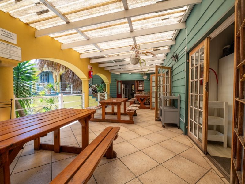 A covered outdoor patio area featuring tiled flooring, timber weatherboard walls, and a translucent roof structure, providing a functional space for outdoor dining.