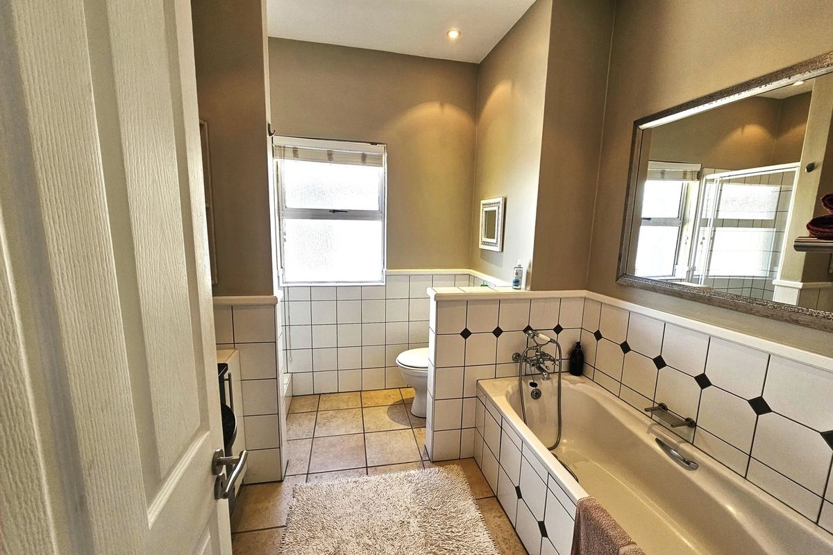 A functional bathroom featuring a built-in bathtub with shower mixer, tiled splashbacks, and a separate toilet area with natural light.