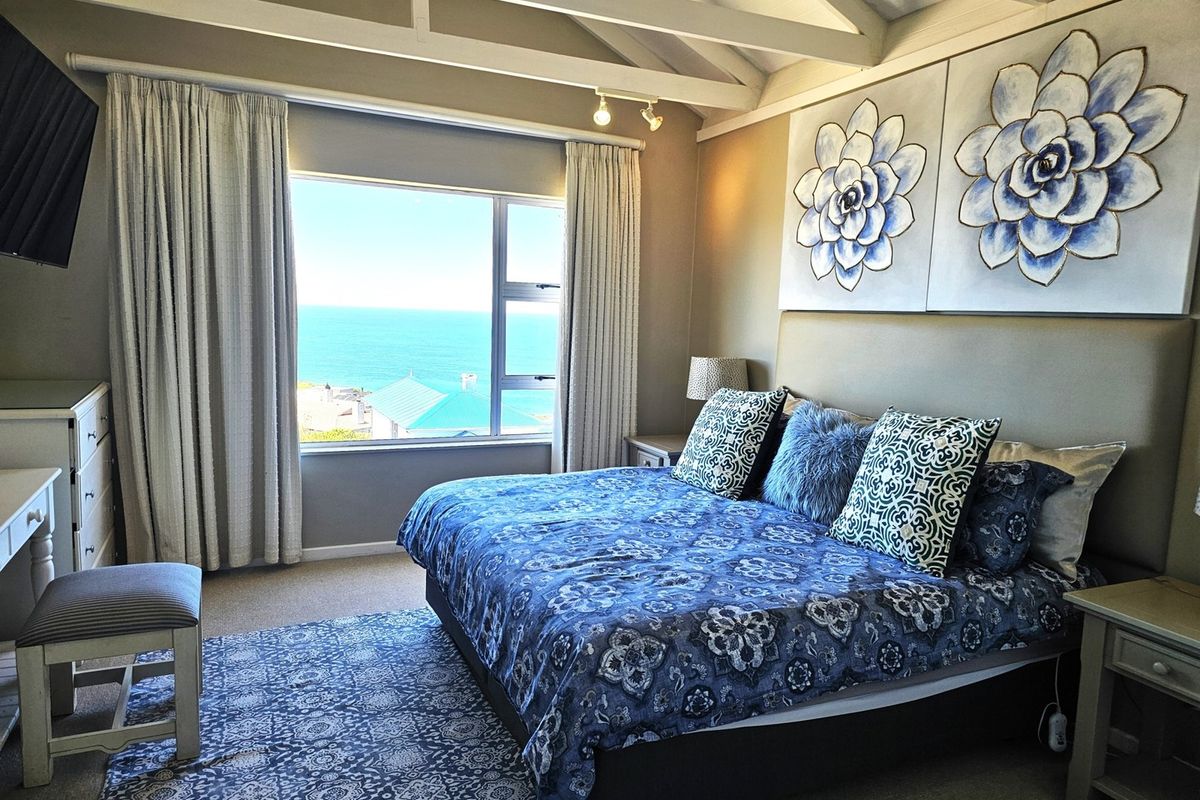 A well-maintained bedroom featuring vaulted ceilings with exposed beams and a large window offering expansive ocean views.
