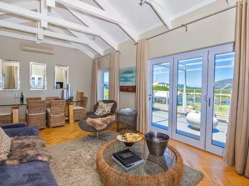 Spacious open-plan living and dining area featuring vaulted ceilings with exposed beams, herringbone parquet flooring, and large glass doors opening to a balcony.