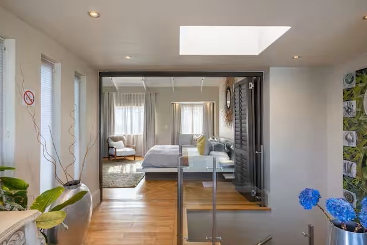 A bright bedroom featuring hardwood flooring, a large skylight, recessed lighting, and a glass balustrade overlooking the lower level.