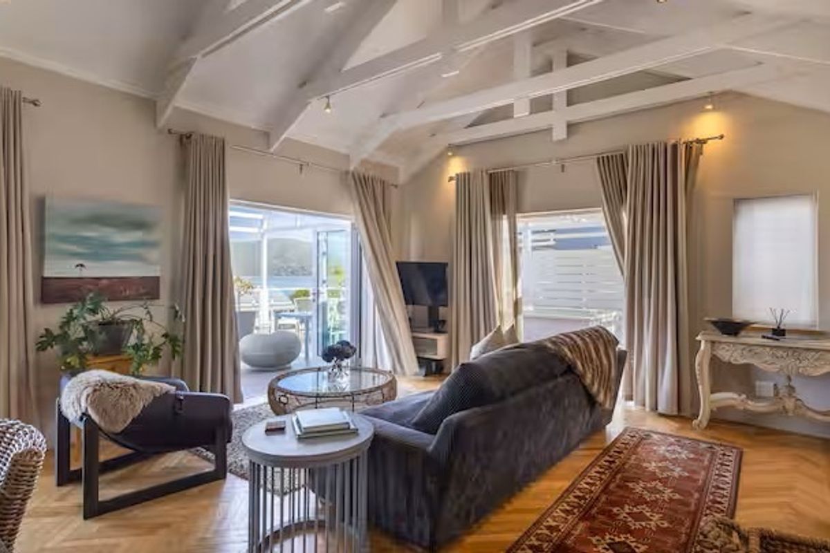 Spacious living room featuring a vaulted ceiling with exposed timber beams, herringbone parquet flooring, and large sliding glass doors leading to an outdoor area.