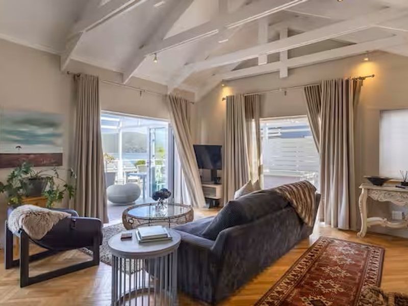 Spacious living room featuring a vaulted ceiling with exposed timber beams, herringbone parquet flooring, and large sliding glass doors leading to an outdoor area.