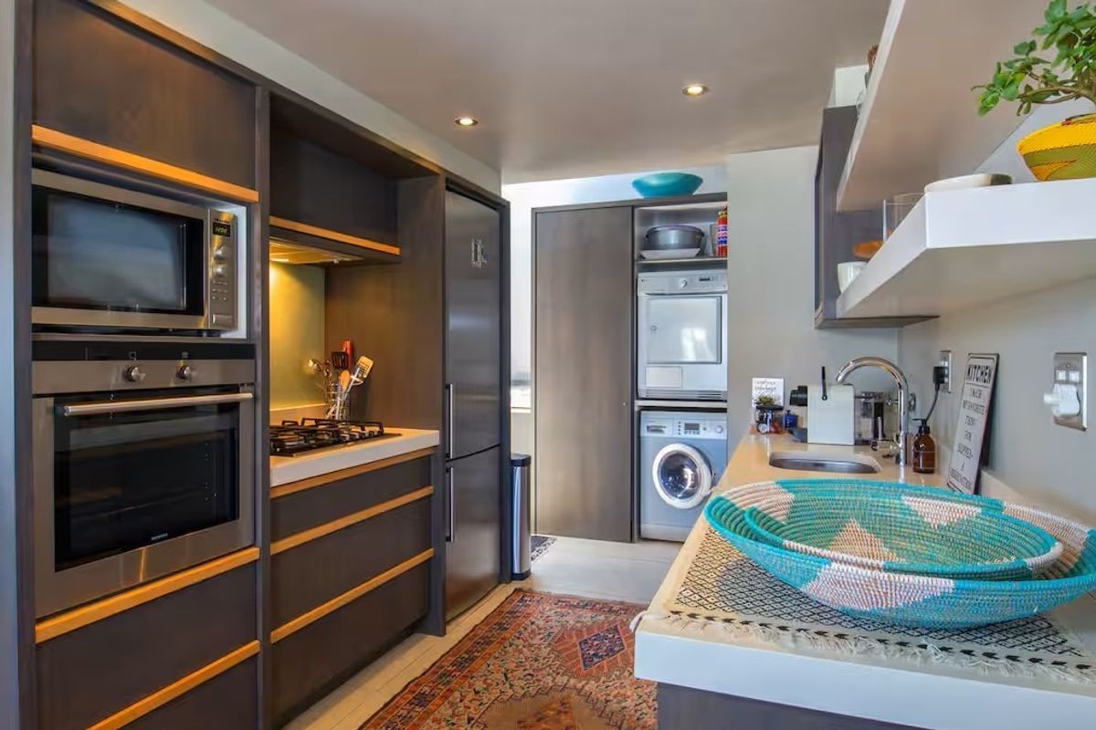 Modern galley-style kitchen featuring dark cabinetry, stone countertops, integrated appliances, and a dedicated laundry nook with built-in washer and dryer.