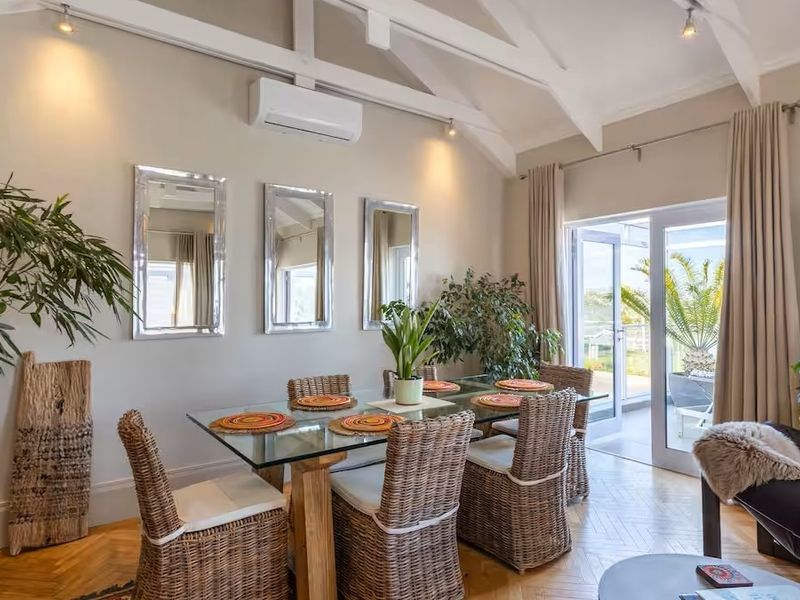 Bright dining room featuring vaulted ceilings with exposed beams, herringbone parquet flooring, and direct access to an outdoor balcony through glass sliding doors.