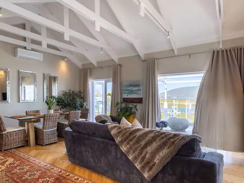 Spacious open-plan living and dining area featuring vaulted ceilings with exposed trusses, elegant herringbone parquet flooring, and large sliding doors leading to a balcony.