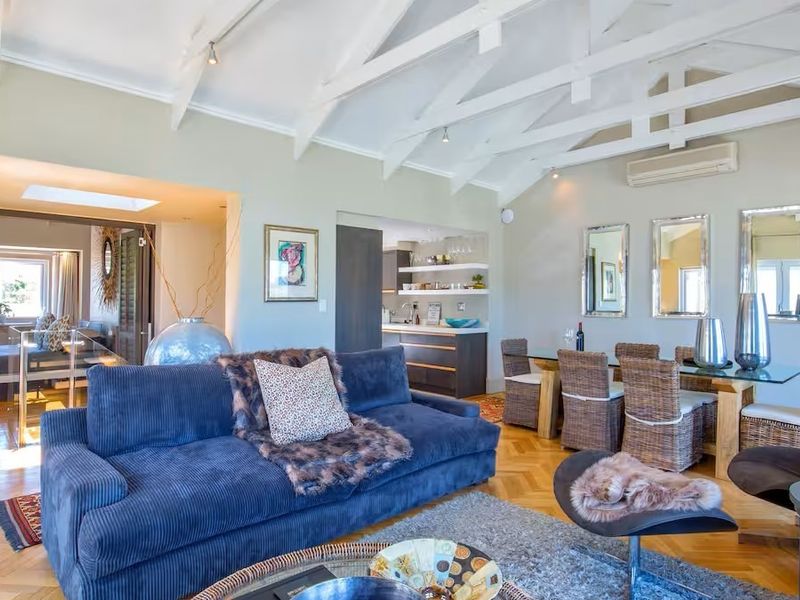 Spacious open-plan living and dining area featuring vaulted ceilings with exposed white trusses, herringbone parquet flooring, and an integrated kitchen space.