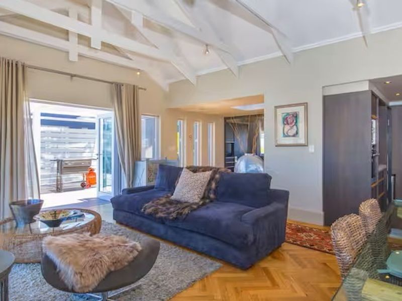Spacious open-plan living area featuring vaulted ceilings with exposed rafters, herringbone parquet flooring, and integrated kitchen and laundry appliances with direct patio access.
