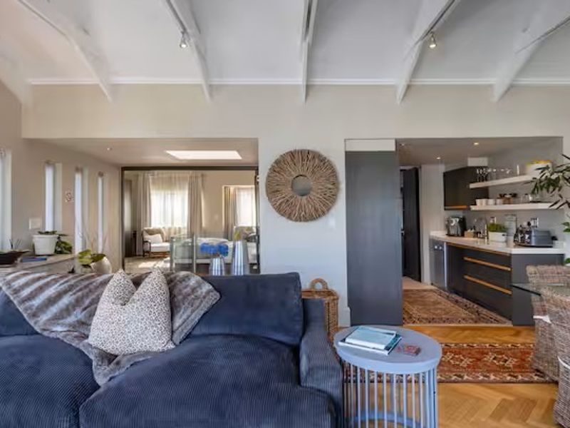 An open-plan living area featuring vaulted ceilings with exposed beams, parquet flooring, and a modern kitchen with integrated cabinetry and a skylight.