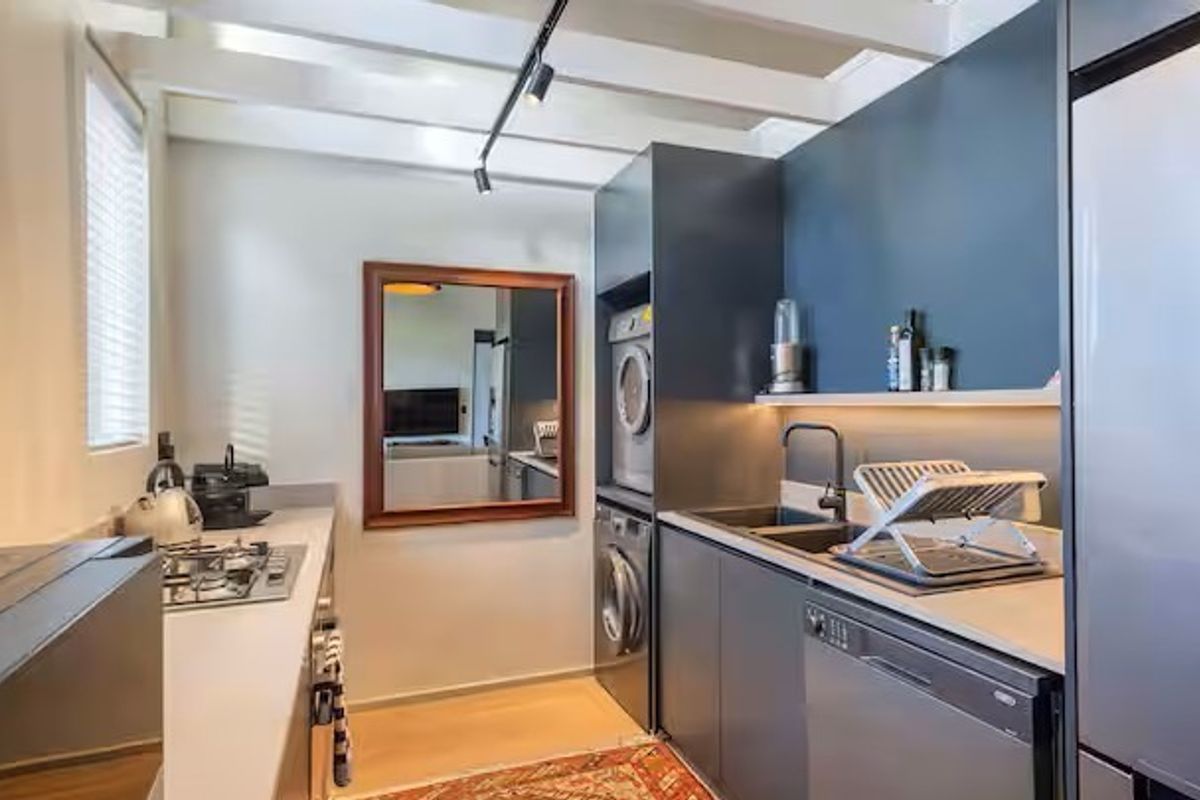 Modern kitchen featuring dark cabinetry, integrated appliances, gas hob, stainless steel sink, and exposed ceiling beams with track lighting.