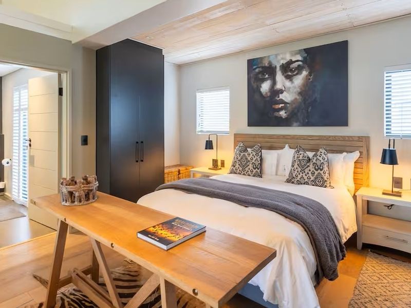 A well-appointed bedroom featuring a timber-clad ceiling, built-in wardrobe, and neutral finishes, with an adjoining en-suite bathroom visible through the doorway.