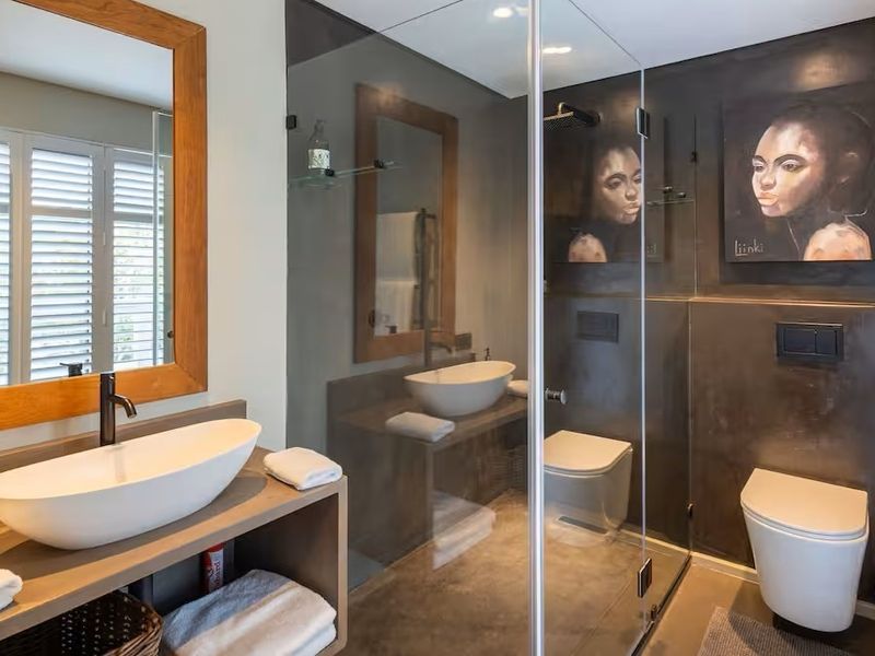 Modern bathroom featuring a vessel sink, wall-hung toilet, walk-in shower with glass enclosure, and stylish dark wall finishes.