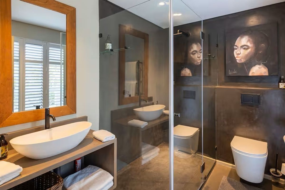 Modern bathroom featuring a vessel sink, wall-hung toilet, walk-in shower with glass enclosure, and stylish dark wall finishes.