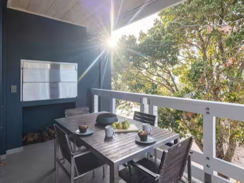 A covered balcony featuring a built-in braai, white railing, and pleasant views of surrounding trees.
