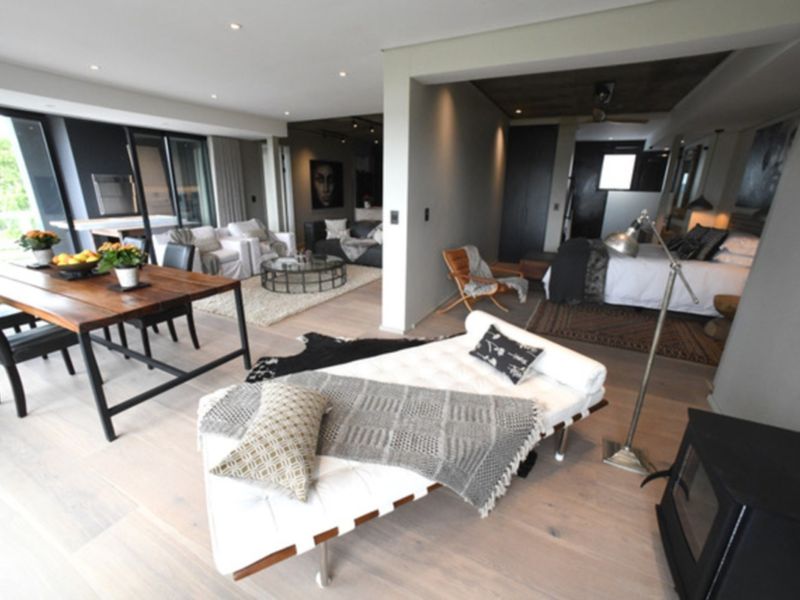 Spacious open-plan living area featuring light hardwood flooring, recessed lighting, a modern wood-burning fireplace, and seamless flow to an adjoining bedroom suite.