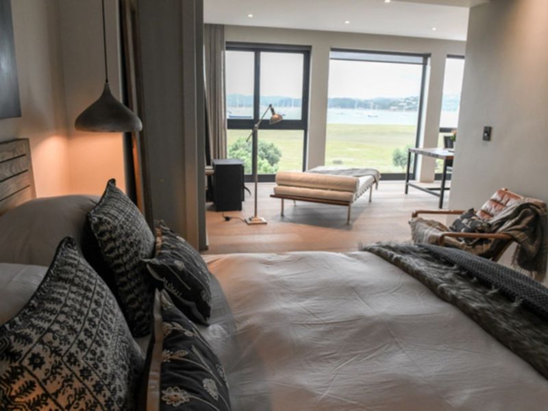 Spacious bedroom featuring high-quality timber flooring, recessed lighting, and large windows offering expansive views of the surrounding landscape.