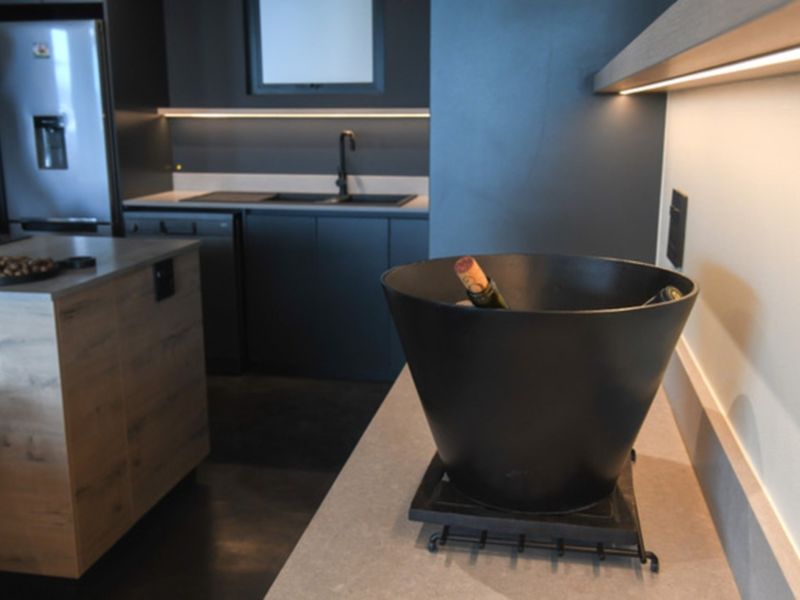 Modern kitchen featuring dark cabinetry, stone countertops, a functional island, and integrated under-cabinet lighting for a sleek, contemporary aesthetic.