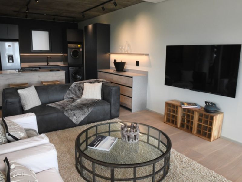 Modern open-plan living area featuring an exposed concrete ceiling, sleek kitchen cabinetry with integrated appliances, and high-quality timber flooring throughout.