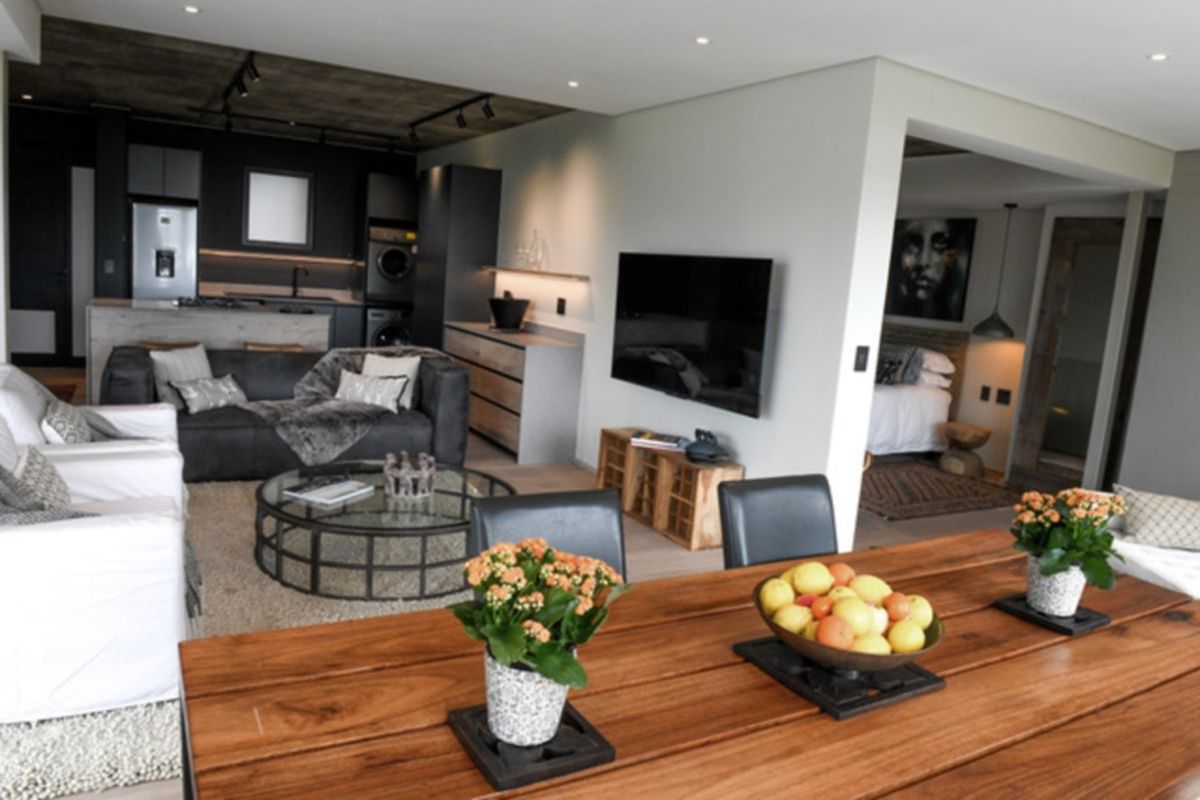 Modern open-plan living area featuring a sleek kitchen with built-in cabinetry, exposed concrete ceilings, and recessed lighting, seamlessly flowing into the dining and lounge space.