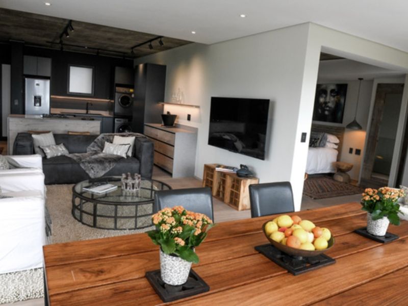 Modern open-plan living area featuring a sleek kitchen with built-in cabinetry, exposed concrete ceilings, and recessed lighting, seamlessly flowing into the dining and lounge space.