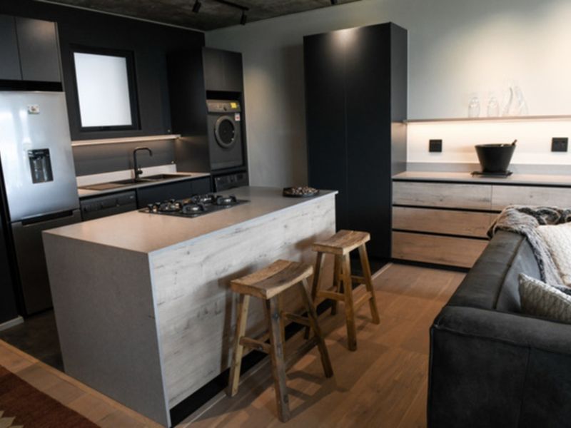 Modern open-plan kitchen featuring a central island with gas cooktop, sleek dark cabinetry, stone countertops, and high-quality integrated appliances.