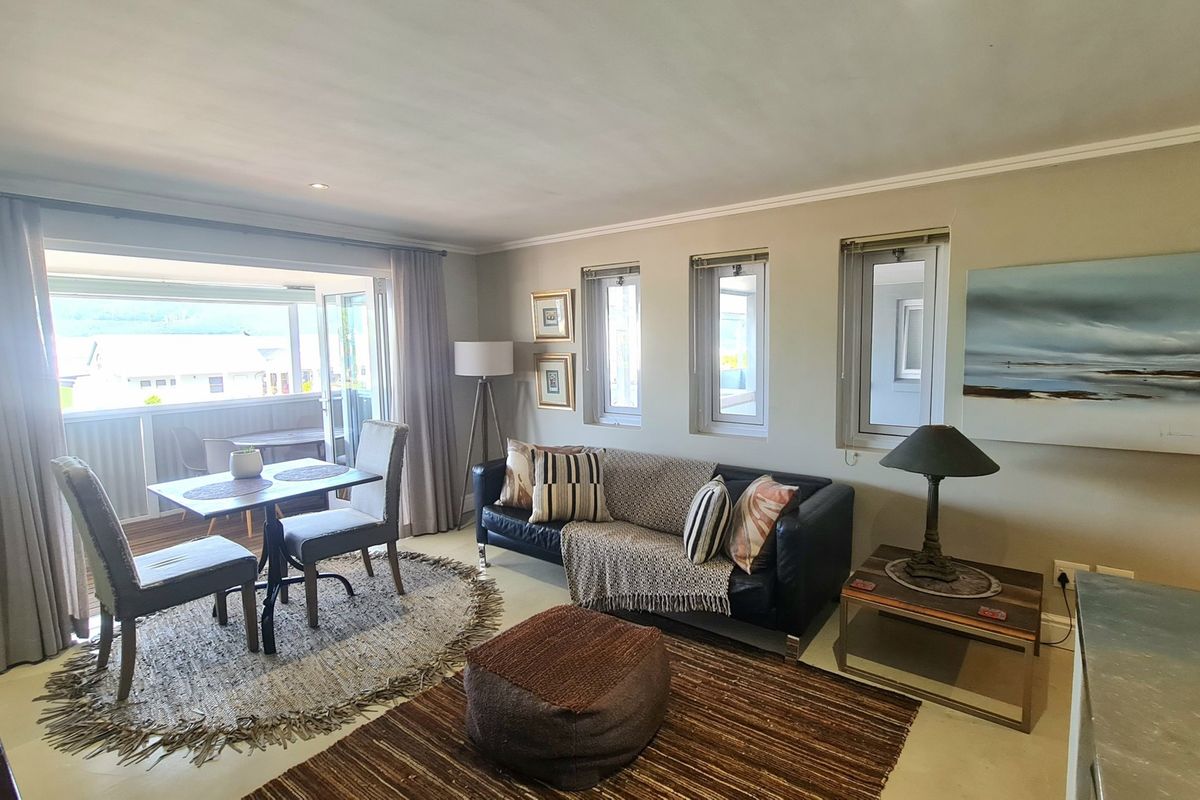 A bright living room featuring neutral walls, cove molding, and large sliding glass doors that open onto a balcony with natural light.