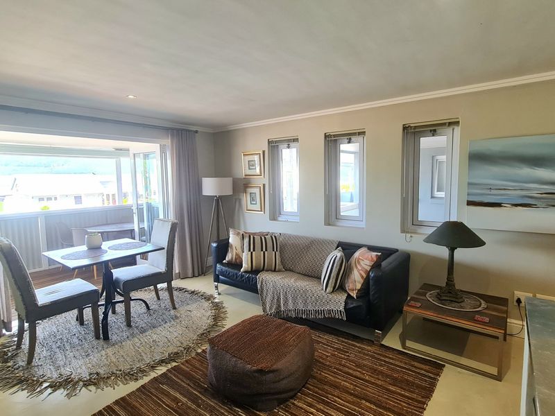 A bright living room featuring neutral walls, cove molding, and large sliding glass doors that open onto a balcony with natural light.