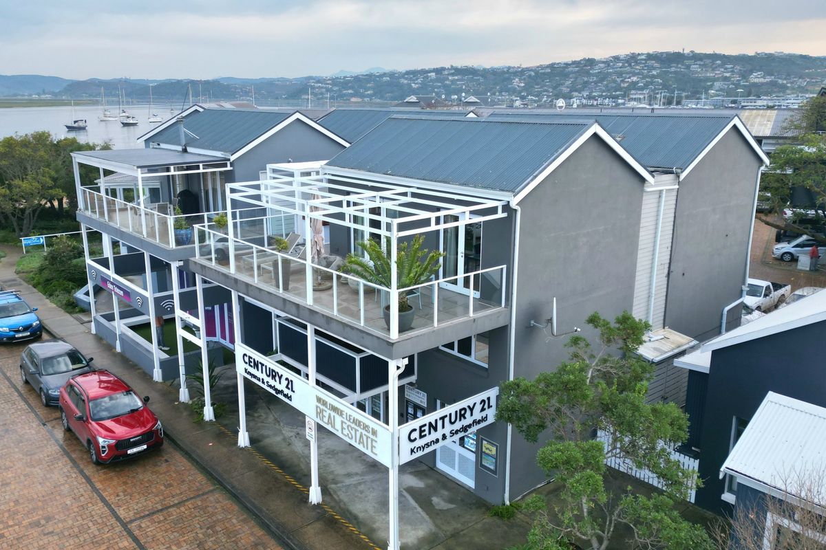 Aerial view of a multi-story apartment building featuring metal roofing, private balconies with glass balustrades, and a paved street-level entrance.