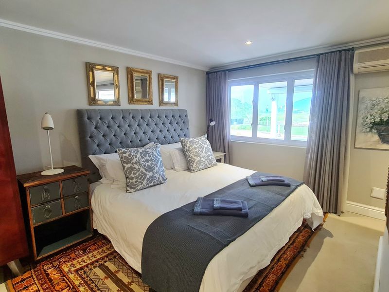 A well-maintained bedroom featuring neutral wall tones, an air conditioning unit, and large windows with floor-to-ceiling curtains.
