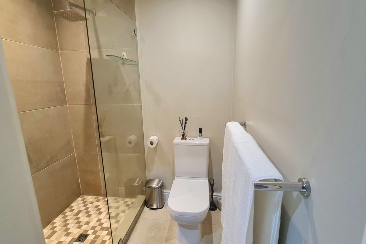 A modern bathroom featuring a walk-in shower with a glass screen, rain shower head, and a wall-mounted towel rail.