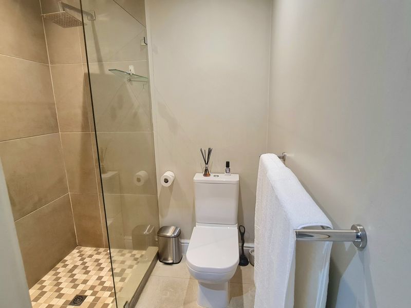 A modern bathroom featuring a walk-in shower with a glass screen, rain shower head, and a wall-mounted towel rail.