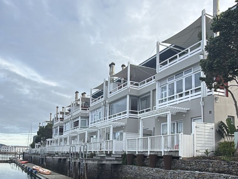 A view of the rear elevation of a waterfront apartment complex featuring multi-level balconies, pergolas, and private jetty access.